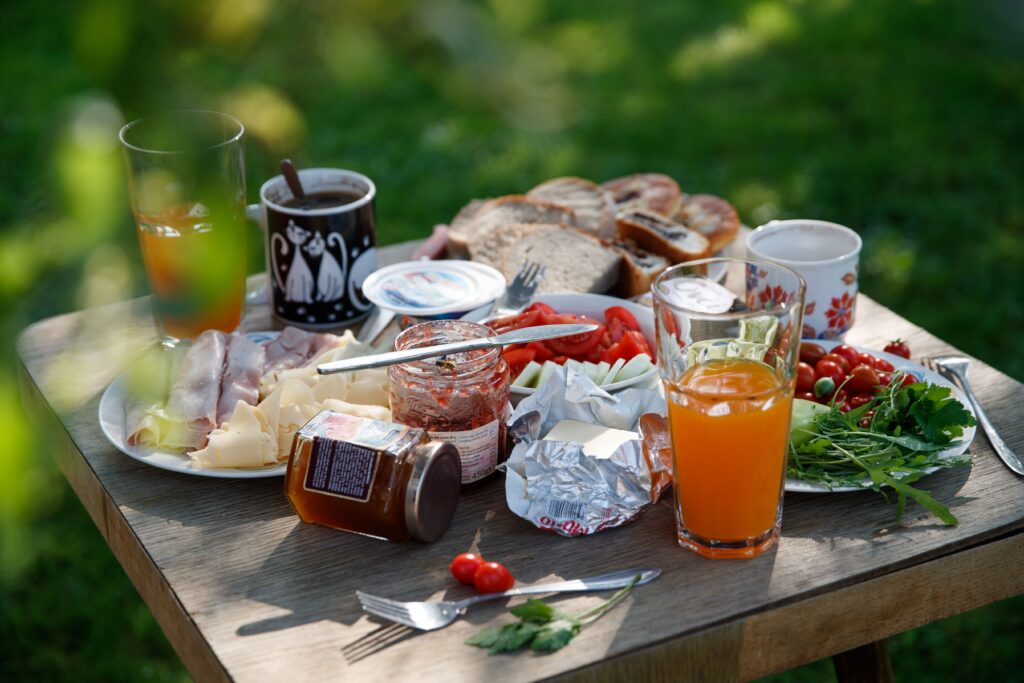 A delightful outdoor picnic table set with bread, cheese, meats, vegetables, and drinks, showcasing a lush summer setting.